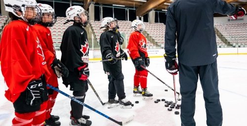 A group of players in hockey gear listening to a coach