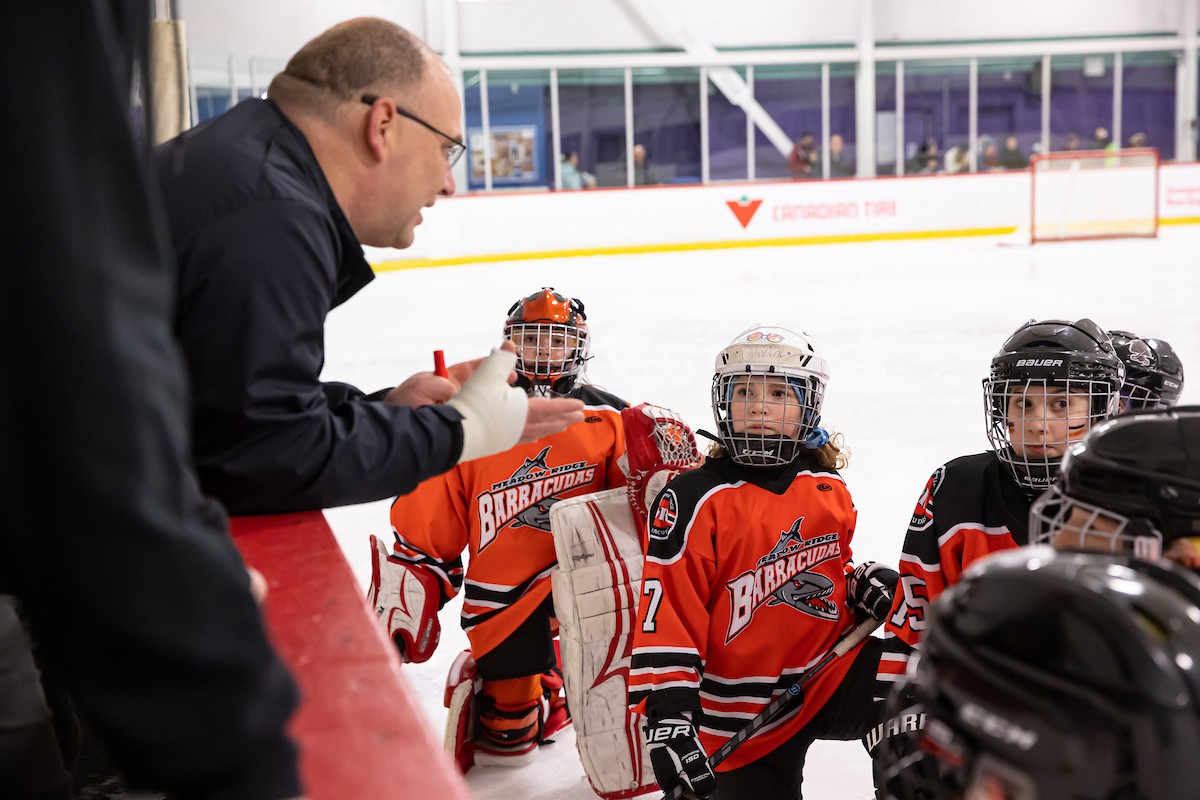 A coach speaking to a group of young players at the boards